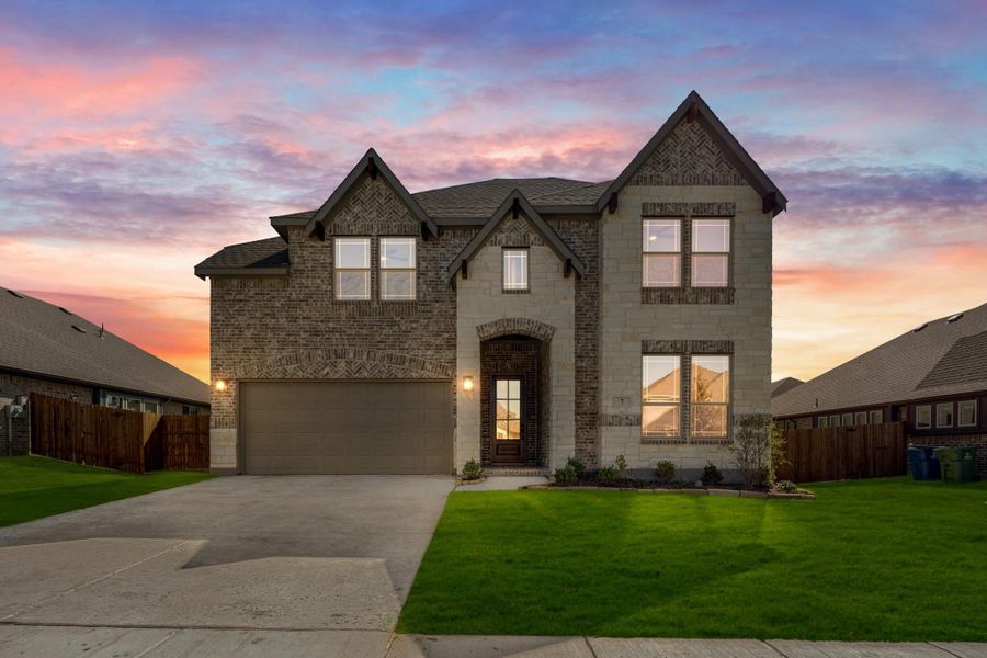 Two-story brick and stone home with two-car garage, arched entry, and green front lawn at dusk Two-story brick and stone home with two-car garage, arched entry, and green front lawn at dusk