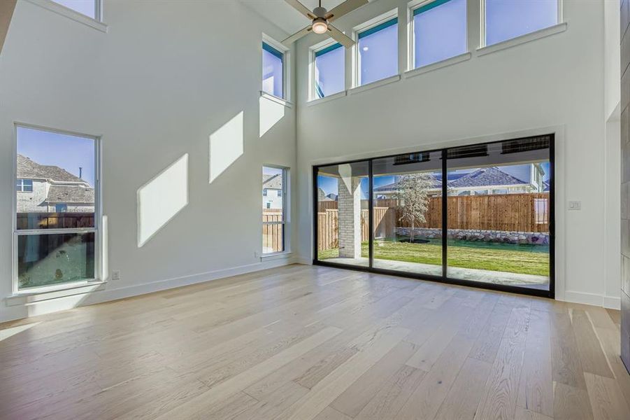 Unfurnished living room featuring light wood-style floors, a high ceiling, and ceiling fan