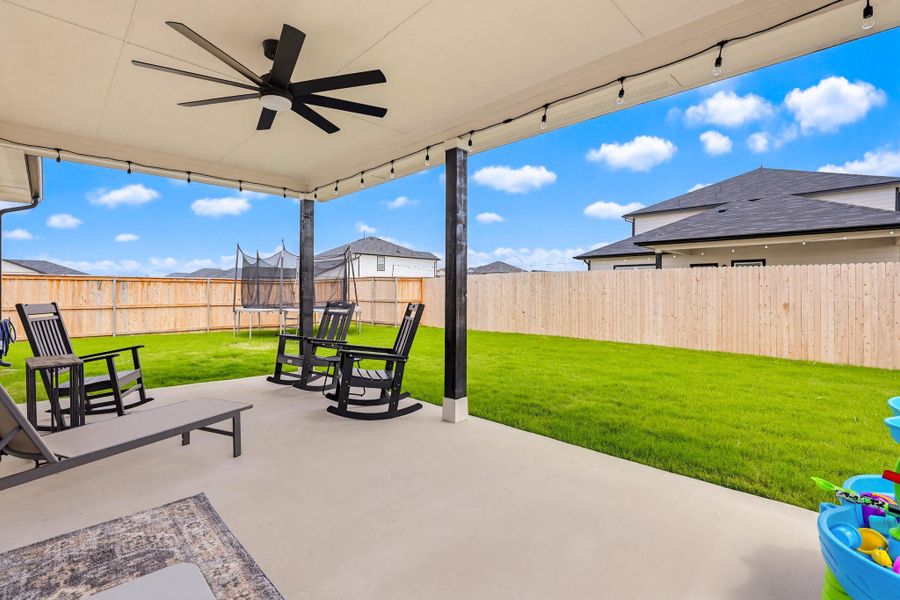 Expansive covered patio featuring a ceiling fan, string lighting, and direct access to a spacious lawn