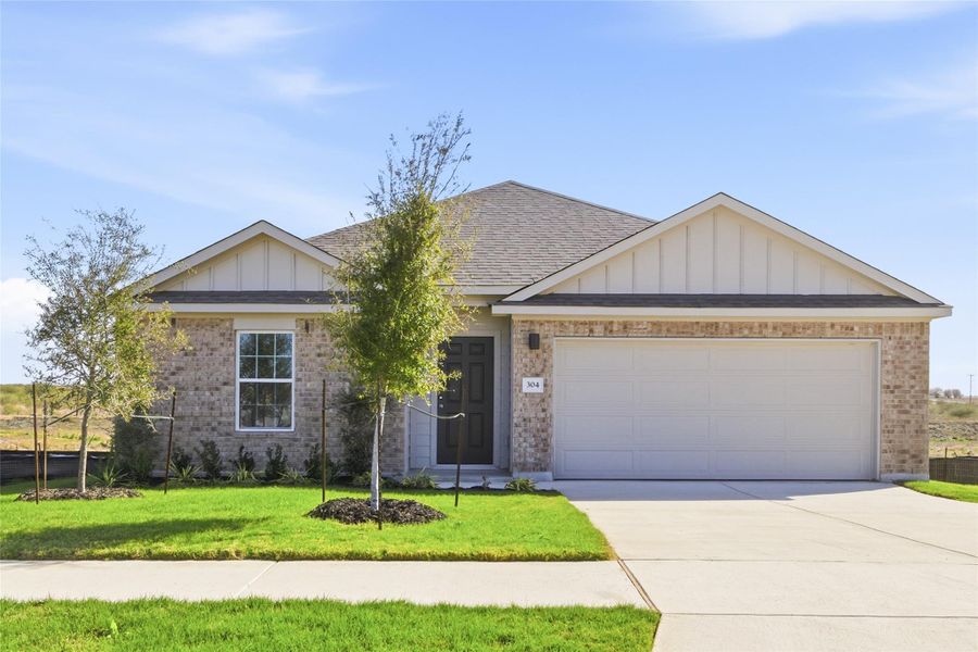 View of front of home featuring board and batten siding, brick siding, an attached garage, and a front yard