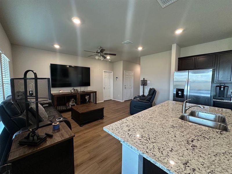 Kitchen with stainless steel refrigerator with ice dispenser, open floor plan, dark wood-style floors, light stone counters, and dark cabinetry