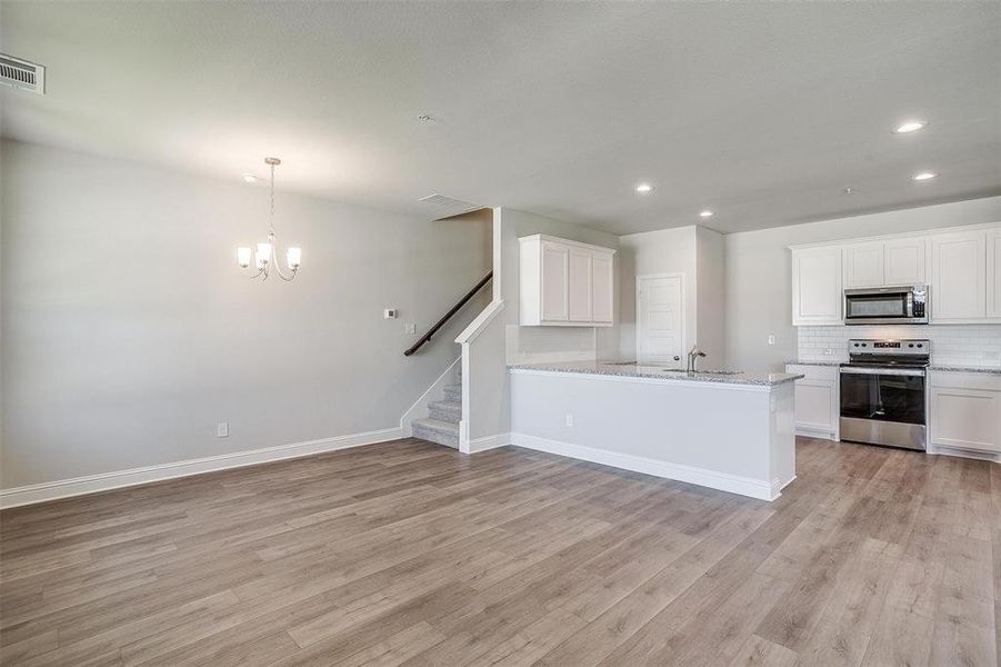 Kitchen featuring stainless steel appliances, white cabinetry, suspended lighting, open floor plan, and light wood-style flooring