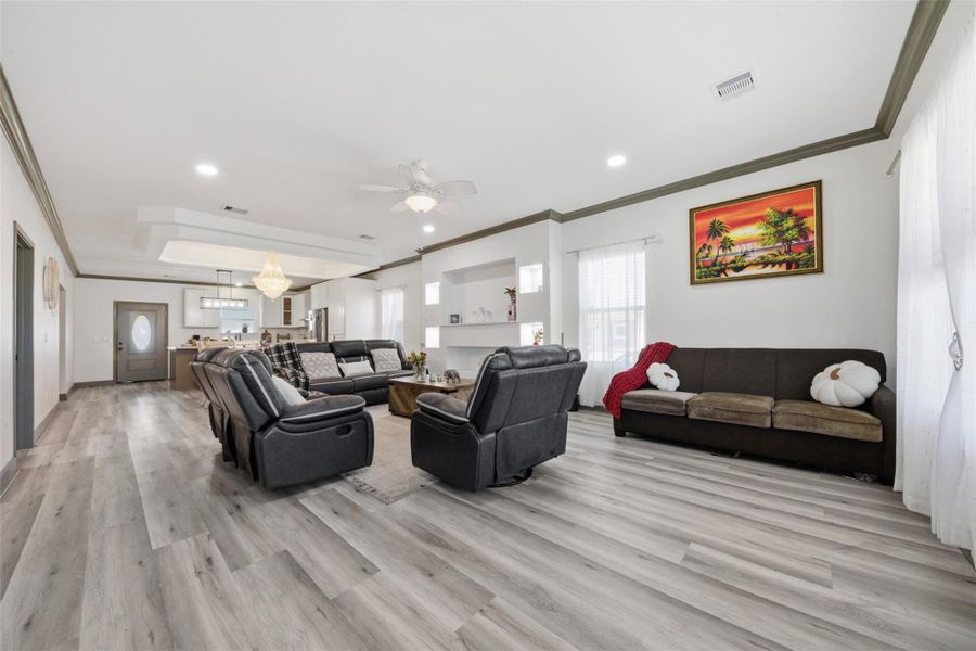 This spacious open-concept living area features modern flooring, ample natural light, and comfortable seating. The room seamlessly connects to the kitchen, creating a perfect space for entertaining. A ceiling fan and stylish lighting add to the inviting atmosphere.