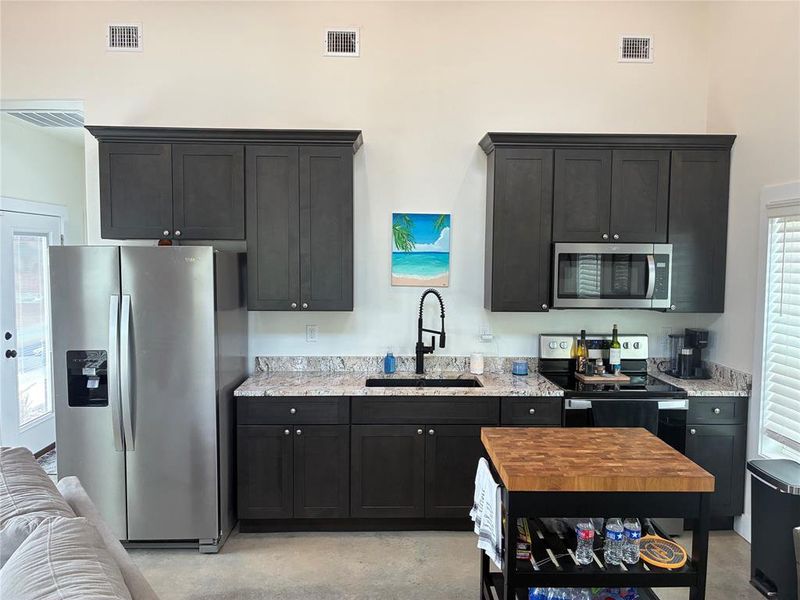 Kitchen with appliances with stainless steel finishes, concrete flooring, dark cabinets, and light stone countertops
