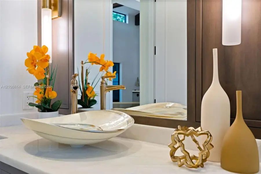 Vanity featuring a stone-surface countertop, vessel sink, metallic-finish faucet, framed mirror, and vertical wall-mounted lighting Vanity featuring a stone-surface countertop, vessel sink, metallic-finish faucet, framed mirror, and vertical wall-mounted lighting