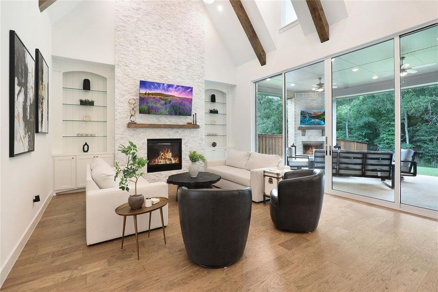 Spacious living area featuring a vaulted ceiling with exposed wood beams, a stone-clad fireplace, and built-in shelving