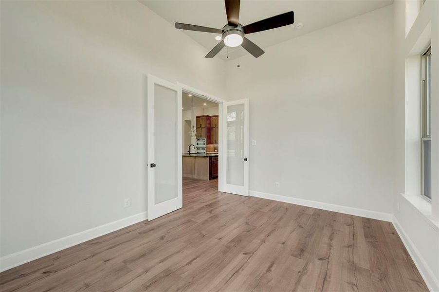 Unfurnished room featuring light wood finished floors, french doors, ceiling fan, and a high ceiling