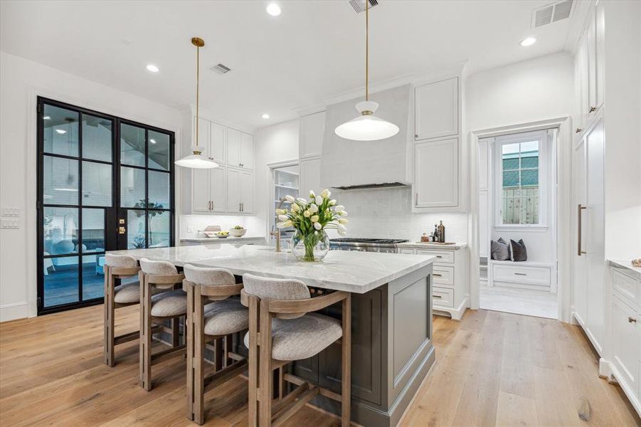 Large kitchen island with quartzite counters, double steel doors leading to patio. Working pantry and mudroom behind kitchen