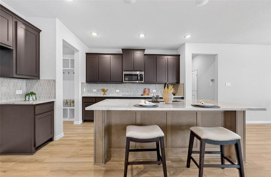 Kitchen featuring dark brown cabinets, light stone counters, a breakfast bar, and recessed lighting Kitchen featuring dark brown cabinets, light stone counters, a breakfast bar, and recessed lighting