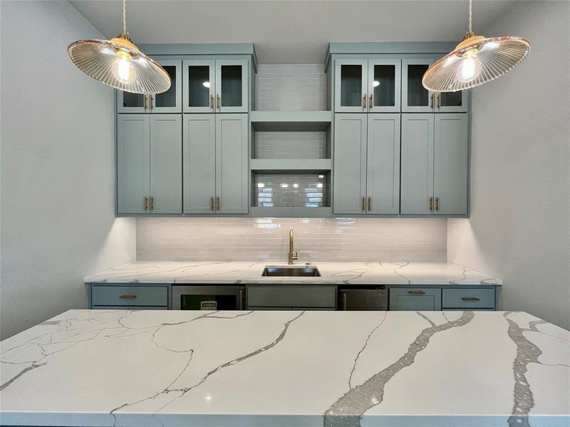 Kitchen with light stone counters, hanging light fixtures, sink, and tasteful backsplash