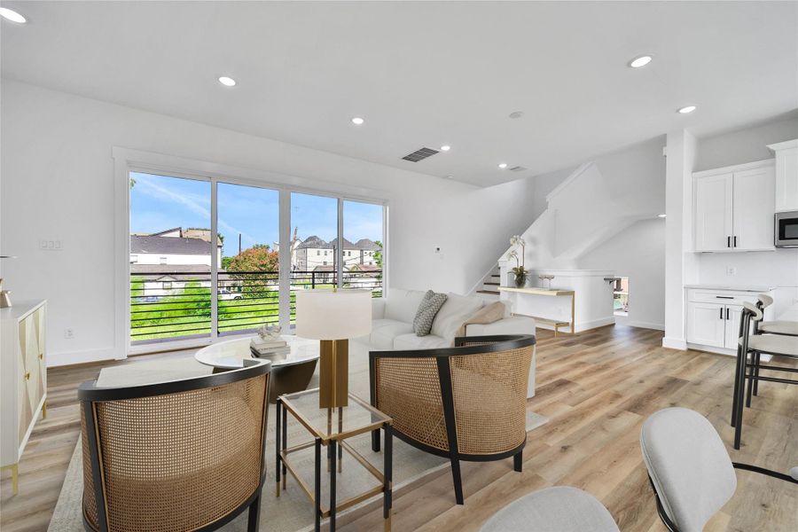 Bright and spacious open-concept living area with modern finishes, large sliding glass doors, and a scenic view. Features include hardwood floors, recessed lighting, and access to a sleek kitchen with white cabinetry. Ideal for comfortable living and entertaining.