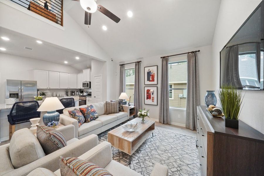 Open-concept living room with vaulted ceiling, white kitchen, and modern furnishings