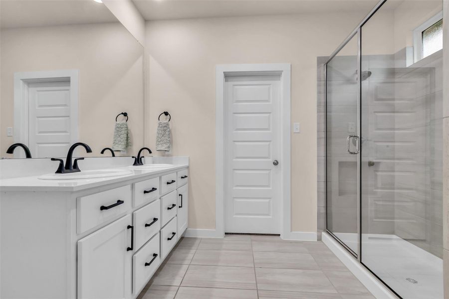 This bathroom features a modern design with a spacious double vanity, sleek black fixtures, and ample drawer storage. It includes a large glass-enclosed shower, neutral tile flooring, and bright, clean lines for a fresh look. This bathroom features a modern design with a spacious double vanity, sleek black fixtures, and ample drawer storage. It includes a large glass-enclosed shower, neutral tile flooring, and bright, clean lines for a fresh look.