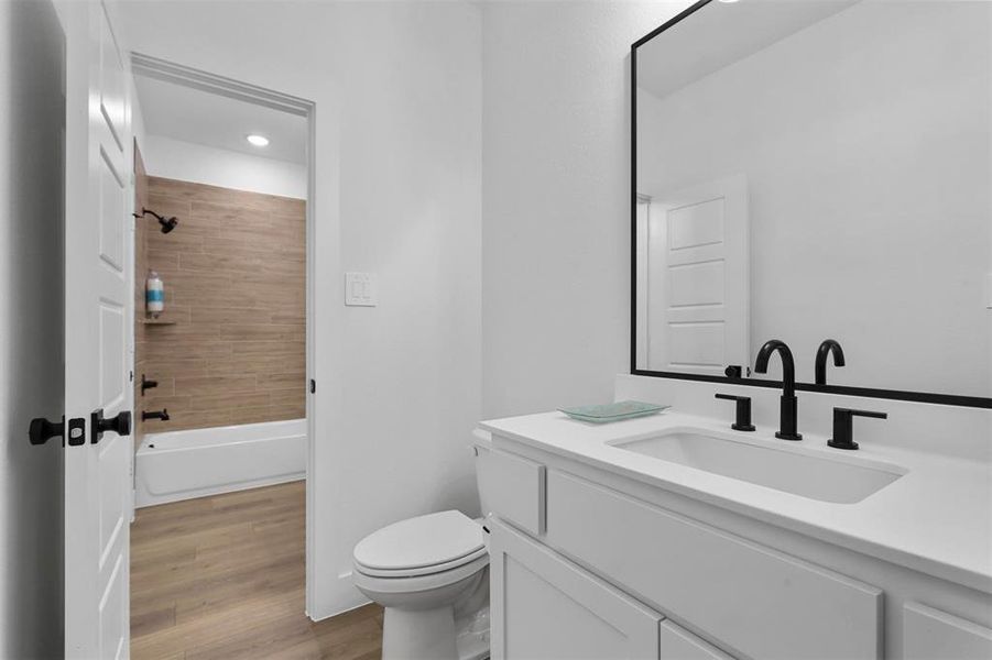 Full bathroom with toilet, tiled shower / bath combo, vanity, and wood-type flooring