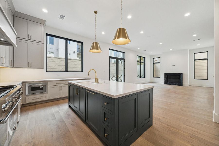 Bianco Superiore Quartzite countertops and backsplash are complemented by Sherwin Williams Accessible Beige cabinets and Sherwin Williams Ripe Olive statement island and complete with cabinet pulls and knobs by Top Knobs Ormonde Collection in honey bronze.