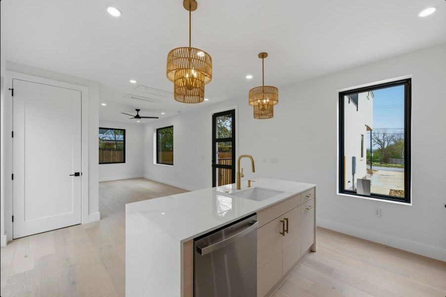 Kitchen with a ceiling fan, dishwasher, a center island with sink, decorative light fixtures, and light stone countertops Kitchen with a ceiling fan, dishwasher, a center island with sink, decorative light fixtures, and light stone countertops