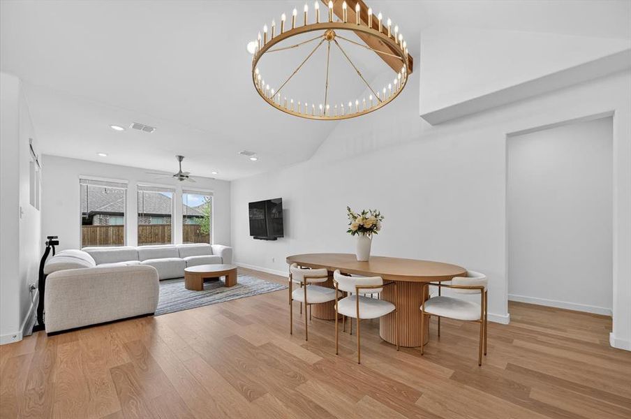 Open-concept living and dining area featuring wood-finish flooring, vaulted ceilings, and a large drum chandelier