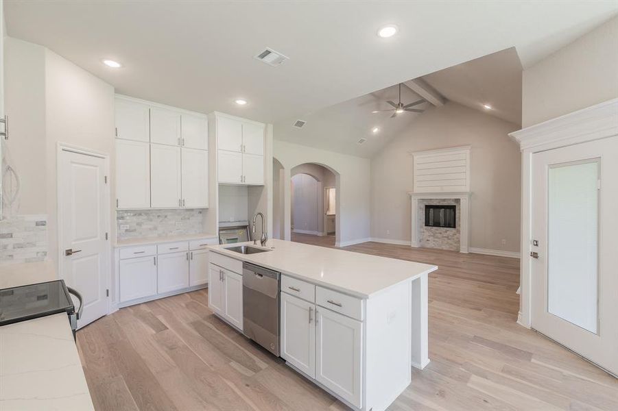 Kitchen featuring light wood-type flooring, sink, dishwasher, vaulted ceiling with beams, and white cabinetry