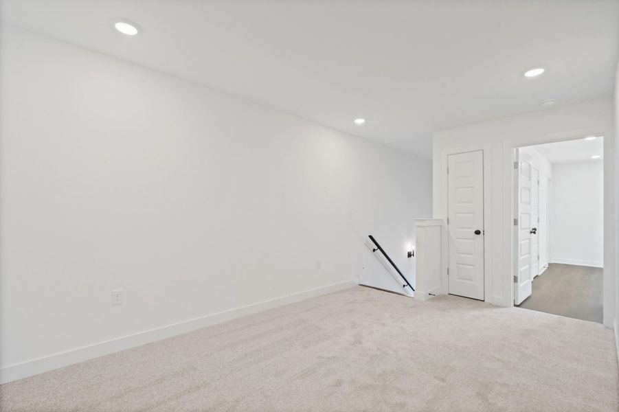 Recessed lighting, light-toned carpeting, white five-panel interior doors, and a black handrail