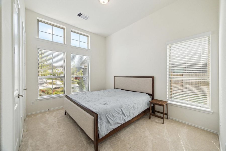 A spacious first-floor secondary bedroom is set at the front of the home, featuring multiple large windows, dual closets, and abundant natural light — ideal for guests or multi-generational living.