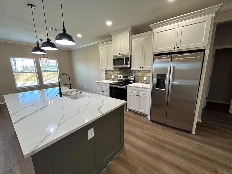 Kitchen featuring stainless steel appliances, decorative backsplash, hanging light fixtures, a center island with sink, and dark wood-style floors