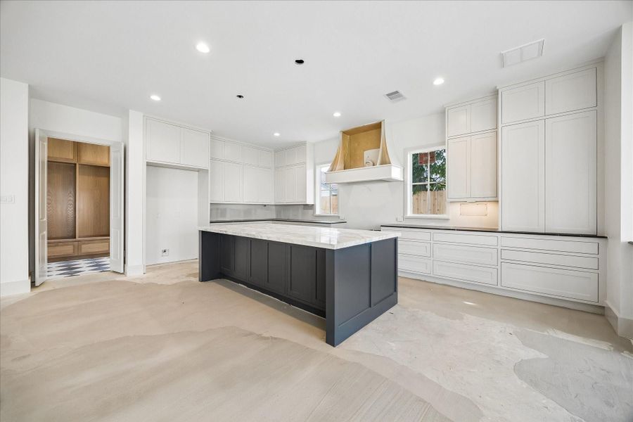 Designer kitchen featuring an oversized island with contrasting dark cabinetry and waterfall style quartz countertops, creating a bold focal point for the space. Surrounded by extensive custom cabinetry, this layout offers abundant storage and prep space, while the open connection to the living area makes it ideal for entertaining. Thoughtful design elements and clean finishes create a modern yet timeless feel.