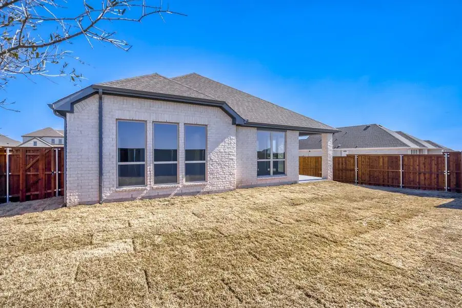 Back of property featuring roof with shingles, brick siding, a fenced backyard, and a patio