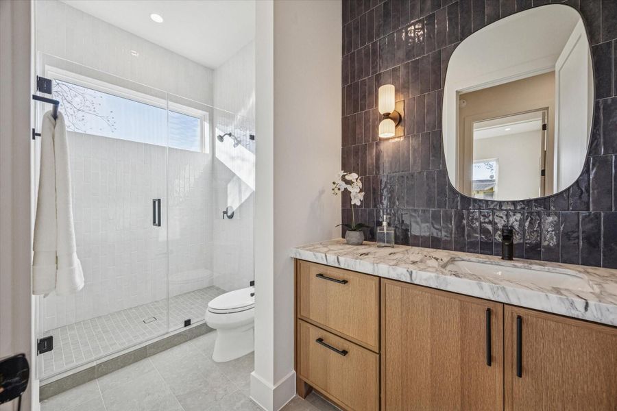 First-floor full bath featuring a glass-enclosed shower, marble countertop with a leathered finish, Italian porcelain tile and stylish lighting.
