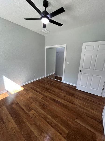 Unfurnished bedroom with dark wood-style flooring, a ceiling fan, a closet, and a textured ceiling Unfurnished bedroom with dark wood-style flooring, a ceiling fan, a closet, and a textured ceiling