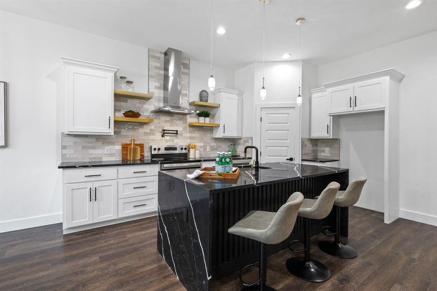 Kitchen featuring stainless steel electric range oven, hanging light fixtures, an island with sink, wall chimney range hood, and white cabinets