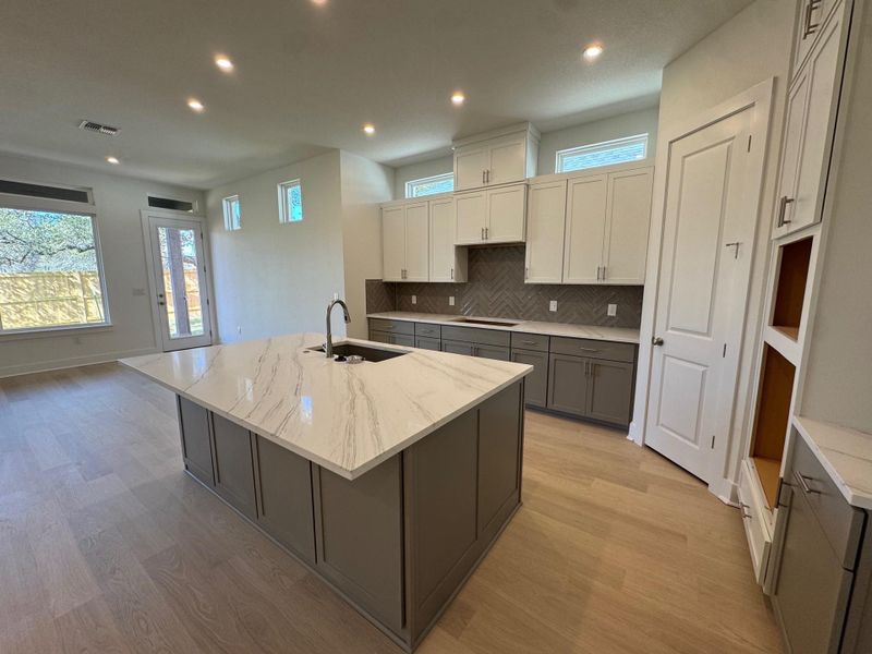 Two tone kitchen featuring a kitchen island with sink, dual tone cabinetry, recessed lighting, light stone countertops, and light wood-type flooring
