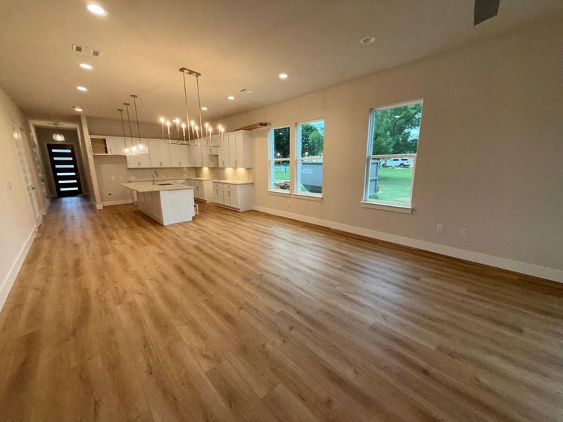 An open-concept living space features light wood-tone flooring and a well-lit kitchen island.