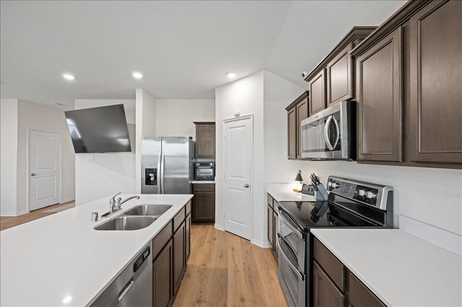 Kitchen featuring stainless steel appliances, light wood-type flooring, dark brown cabinets, recessed lighting, and a center island with sink Kitchen featuring stainless steel appliances, light wood-type flooring, dark brown cabinets, recessed lighting, and a center island with sink
