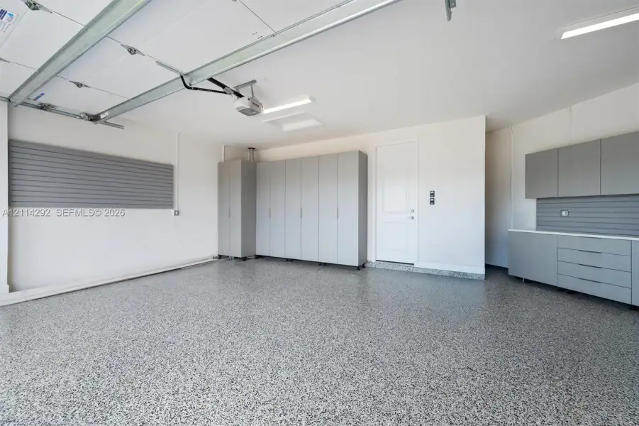 Finished garage featuring speckled epoxy flooring, built-in grey cabinetry, wall-mounted storage panels, and overhead LED lighting