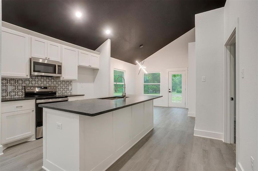 Kitchen with appliances with stainless steel finishes, dark countertops, white cabinets, high vaulted ceiling, and light wood-style flooring