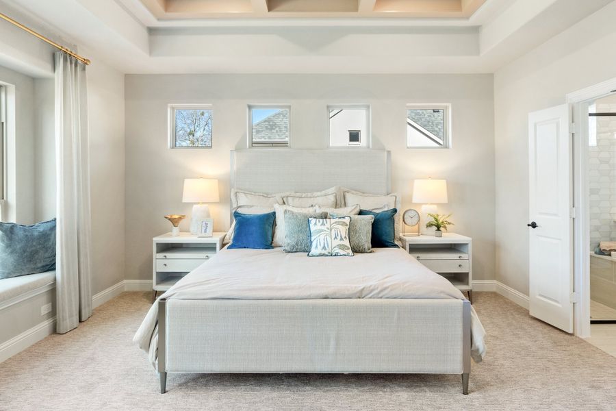 Master bedroom with coffered ceiling, upholstered bed, white nightstands, and ensuite bathroom door Master bedroom with coffered ceiling, upholstered bed, white nightstands, and ensuite bathroom door
