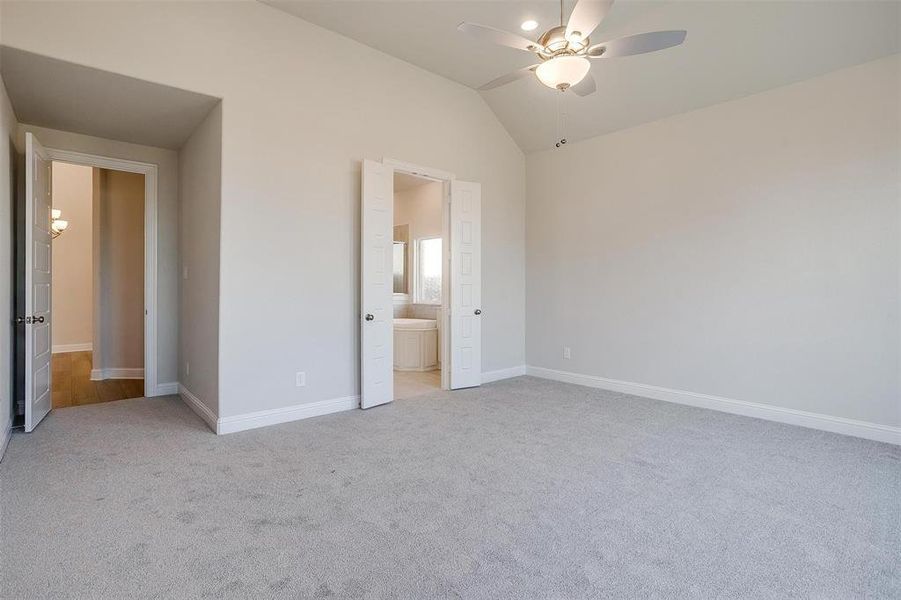 Unfurnished bedroom featuring ceiling fan, lofted ceiling, ensuite bathroom, and light carpet