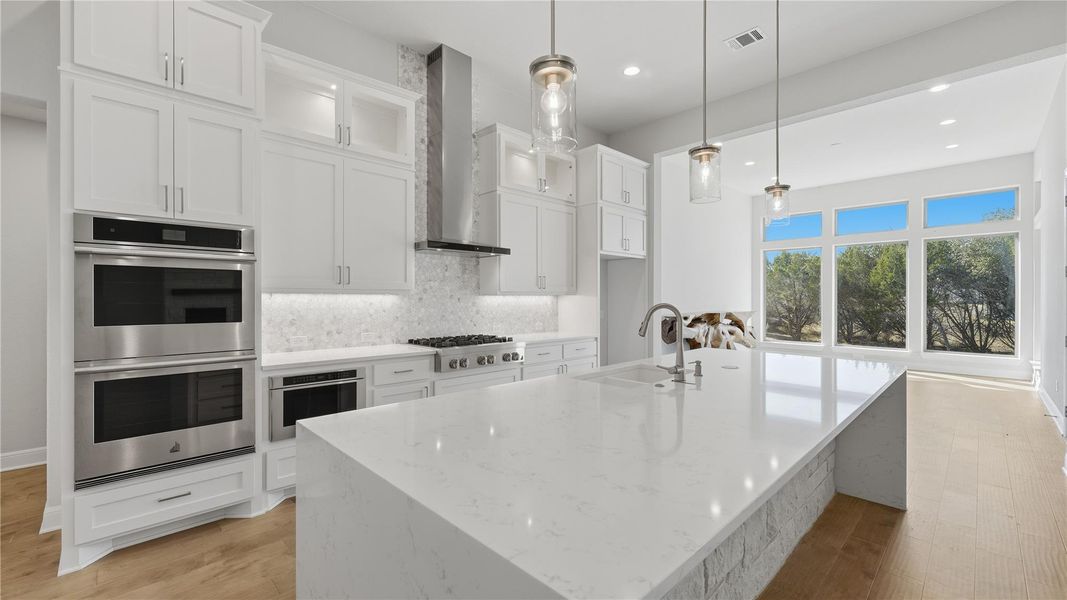 Kitchen with white cabinetry, stainless steel appliances, light stone counters, glass insert cabinets, and recessed lighting Kitchen with white cabinetry, stainless steel appliances, light stone counters, glass insert cabinets, and recessed lighting