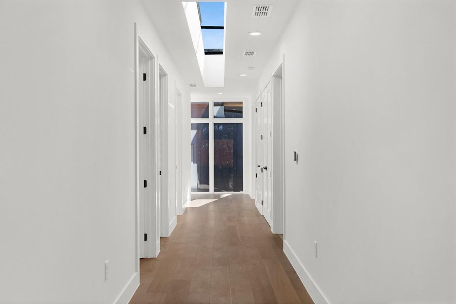 Hallway with recessed lighting, a skylight, and wood finished floors Hallway with recessed lighting, a skylight, and wood finished floors