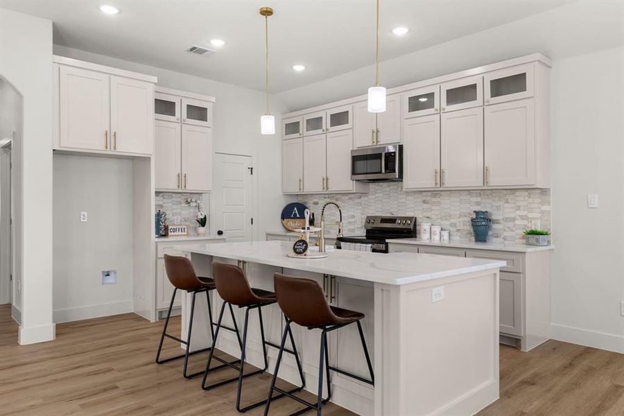 Kitchen featuring decorative light fixtures, white cabinets, a kitchen island with sink, light hardwood / wood-style floors, and stainless steel appliances