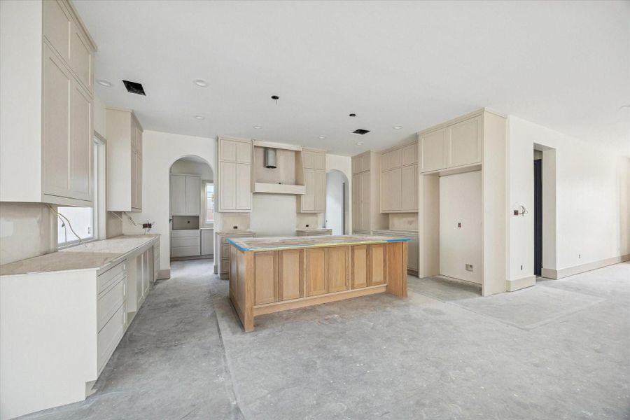 KITCHEN - Soft neutral cabinetry rises to the ceiling, creating a clean, cohesive backdrop for the space, while a warm wood island adds contrast and scale at the center. Arched openings, generous storage, and thoughtful layout details highlight a kitchen designed for both daily use and elevated entertaining. -- Construction as of 1/5/26