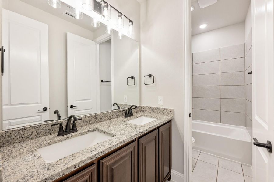 Bathroom with double sink granite vanity, dark wood cabinets, and tiled bathtub surround Bathroom with double sink granite vanity, dark wood cabinets, and tiled bathtub surround