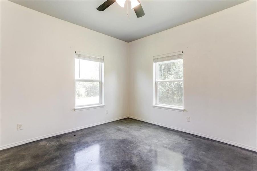 Spacious room featuring two large windows, a ceiling fan, and polished concrete flooring