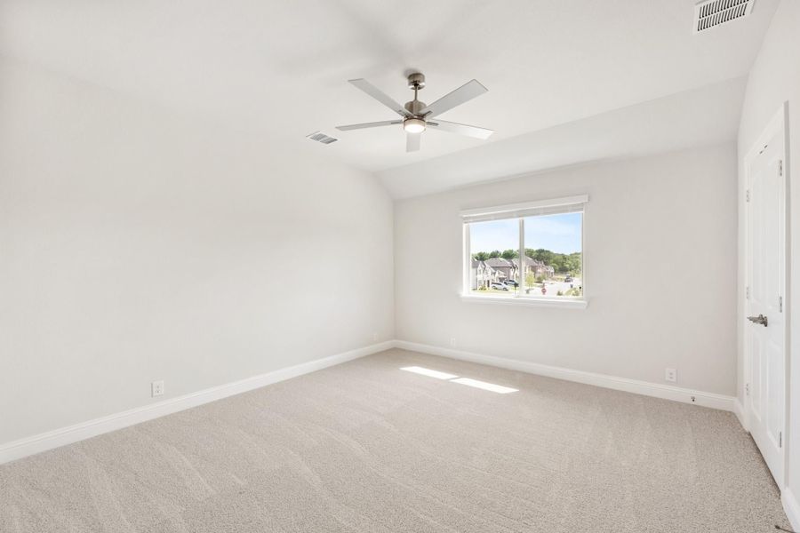 Empty bedroom with vaulted ceiling, ceiling fan, carpet flooring, and a window overlooking the neighborhood