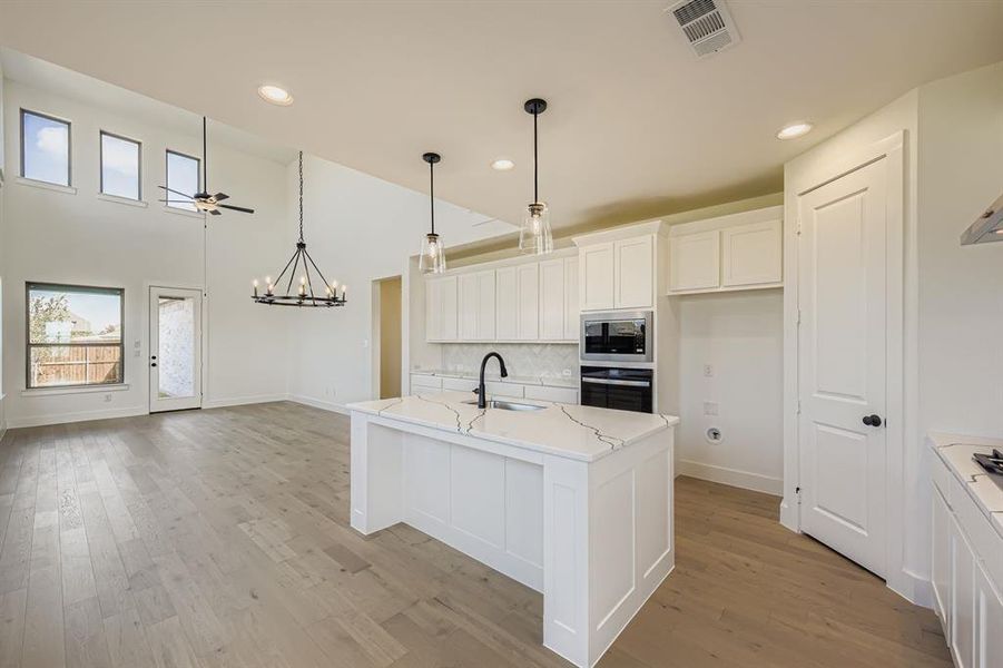 Kitchen with white cabinetry, decorative backsplash, a kitchen island with sink, pendant lighting, and appliances with stainless steel finishes