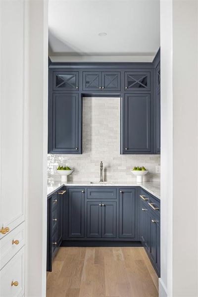Kitchen with light stone counters, light wood-style floors, decorative backsplash, and blue cabinets Kitchen with light stone counters, light wood-style floors, decorative backsplash, and blue cabinets