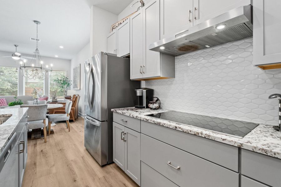 Kitchen featuring appliances with stainless steel finishes, light wood finished floors, a ceiling fan, tasteful backsplash, and under cabinet range hood Kitchen featuring appliances with stainless steel finishes, light wood finished floors, a ceiling fan, tasteful backsplash, and under cabinet range hood