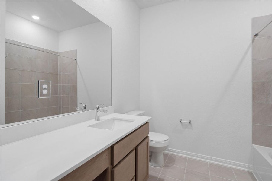 The secondary bathroom showcases tile flooring, a bath/shower combo with tile surround, a vanity with knee space and a stunning light countertop, a vanity mirror, sleek fixtures, and contemporary finishes throughout.