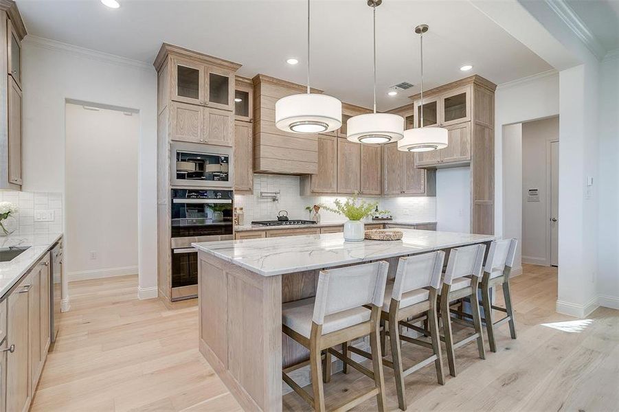 Kitchen featuring Quartzite countertops, tasteful backsplash, light hardwood / wood-style flooring, a kitchen island, and appliances with stainless steel finishes