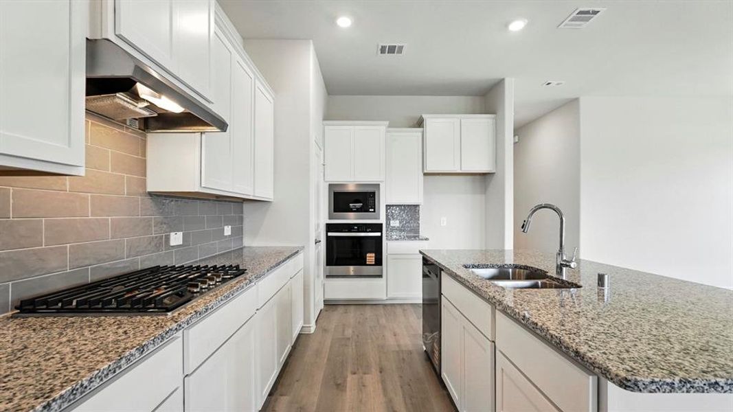 Kitchen featuring white cabinetry, granite countertops, wood-finish flooring, stainless steel appliances, and a subway tile backsplash Kitchen featuring white cabinetry, granite countertops, wood-finish flooring, stainless steel appliances, and a subway tile backsplash